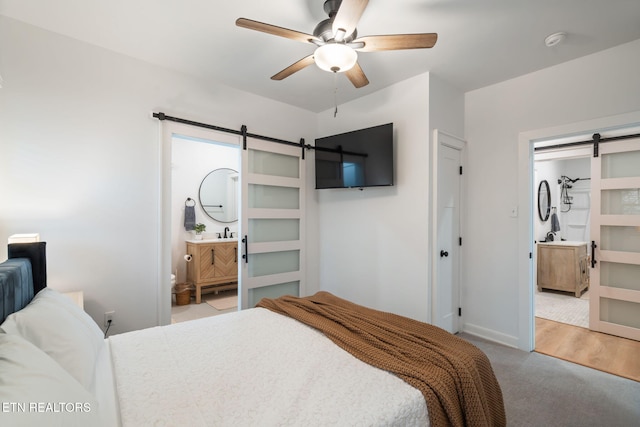 bedroom featuring a barn door, baseboards, a ceiling fan, and ensuite bathroom