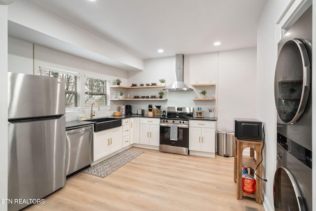 kitchen with open shelves, a sink, stainless steel appliances, wall chimney range hood, and stacked washer / drying machine