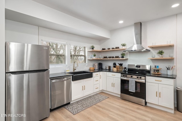 kitchen featuring open shelves, a sink, appliances with stainless steel finishes, wall chimney exhaust hood, and light wood-type flooring