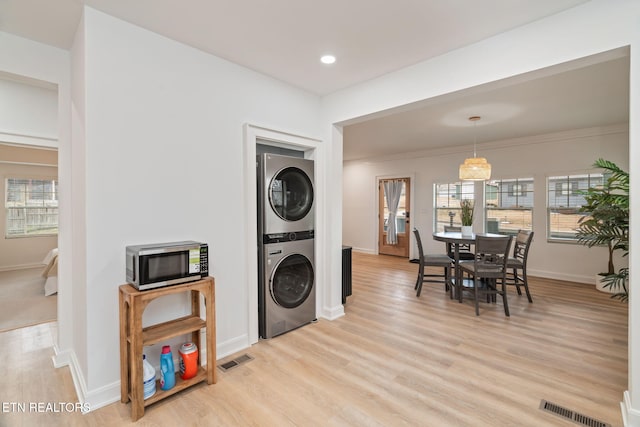 kitchen with baseboards, visible vents, stainless steel microwave, stacked washer / dryer, and light wood-type flooring