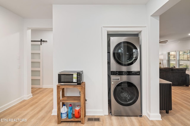 washroom with a barn door, wood finished floors, stacked washer and clothes dryer, and laundry area