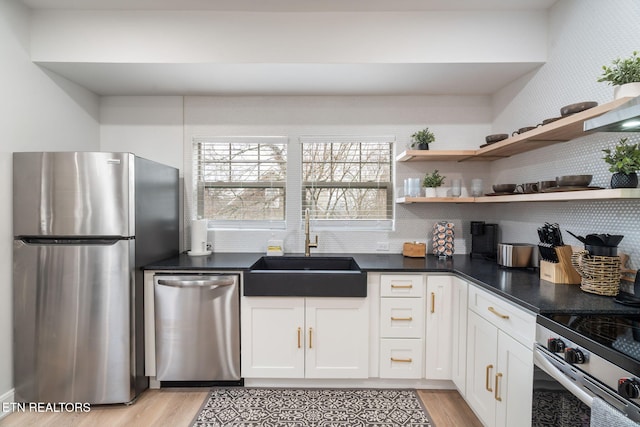 kitchen with light wood-style flooring, a sink, dark countertops, appliances with stainless steel finishes, and white cabinets