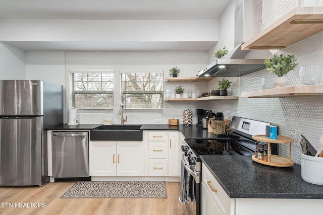 kitchen featuring a sink, white cabinetry, light wood-style floors, appliances with stainless steel finishes, and wall chimney exhaust hood