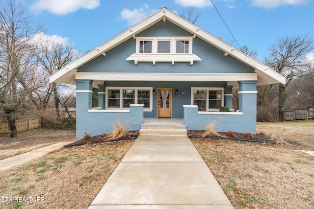 bungalow-style home with stucco siding, a porch, and fence