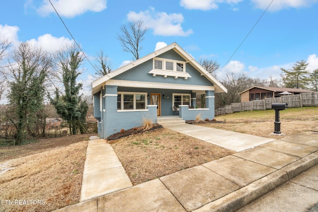 view of front of house featuring stucco siding, covered porch, a front lawn, and fence