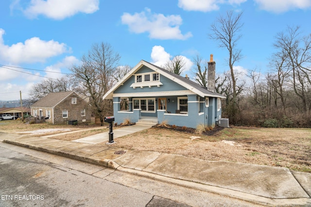 bungalow with cooling unit, a porch, a chimney, and stucco siding