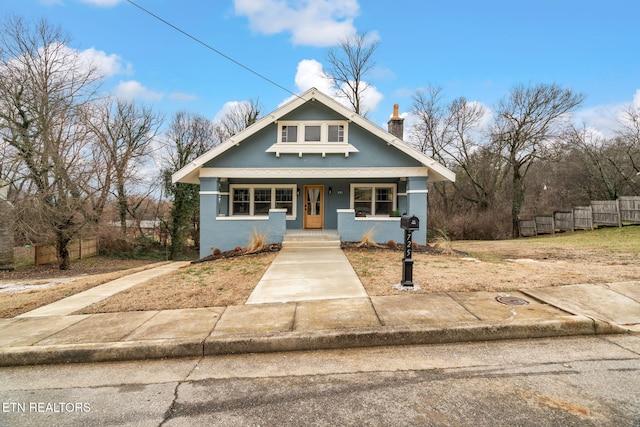 view of front of house featuring stucco siding, fence, covered porch, and a chimney