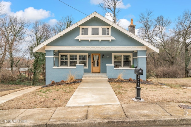 bungalow-style house featuring stucco siding, covered porch, and a chimney