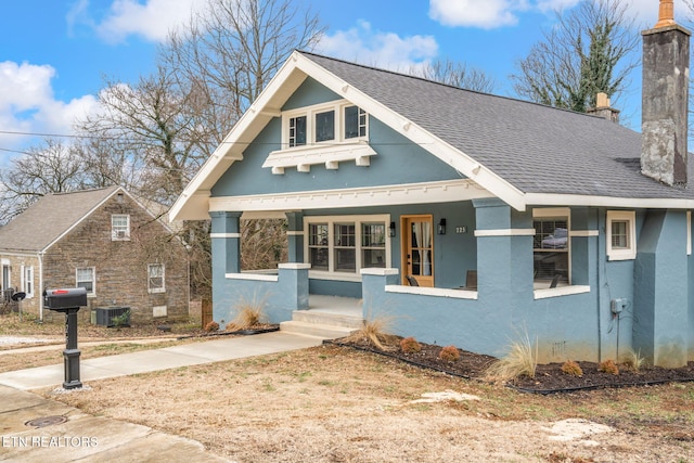 view of front facade with stucco siding, central AC, covered porch, roof with shingles, and a chimney