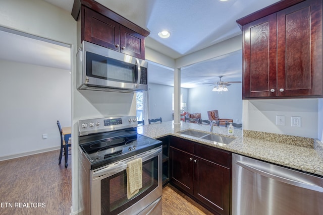 kitchen featuring a sink, light wood-style floors, appliances with stainless steel finishes, light stone countertops, and ceiling fan