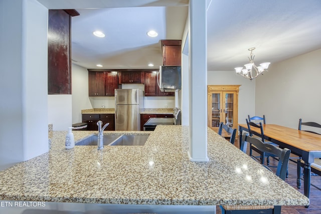 kitchen with reddish brown cabinets, light stone counters, freestanding refrigerator, electric stove, and a sink