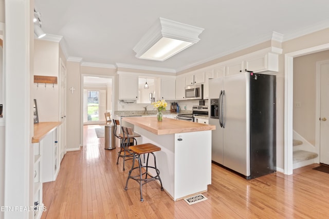 kitchen featuring white cabinets, appliances with stainless steel finishes, crown molding, and a kitchen breakfast bar