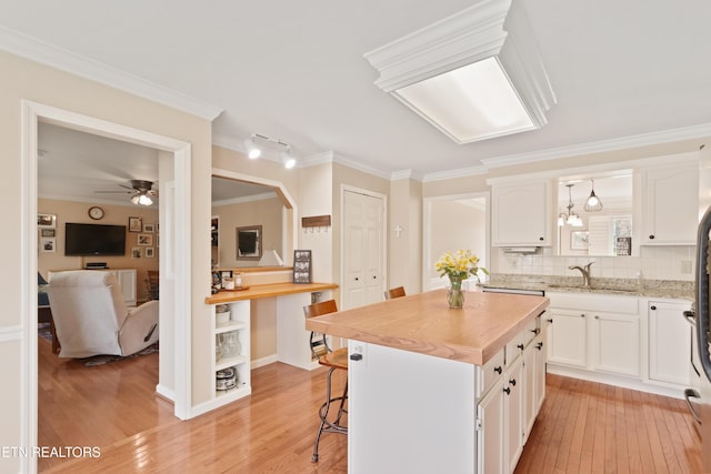 kitchen with light wood finished floors, a sink, white cabinets, crown molding, and butcher block counters