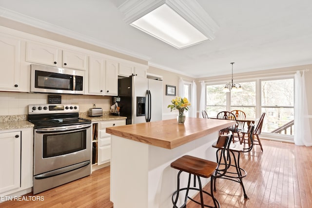 kitchen with wood counters, white cabinetry, stainless steel appliances, crown molding, and light wood finished floors