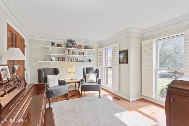 living area featuring a healthy amount of sunlight, wood finished floors, visible vents, and ornamental molding