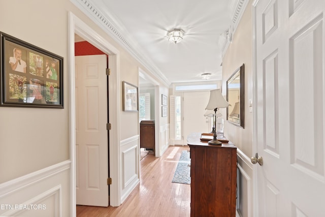 hall with crown molding, a decorative wall, light wood finished floors, and wainscoting