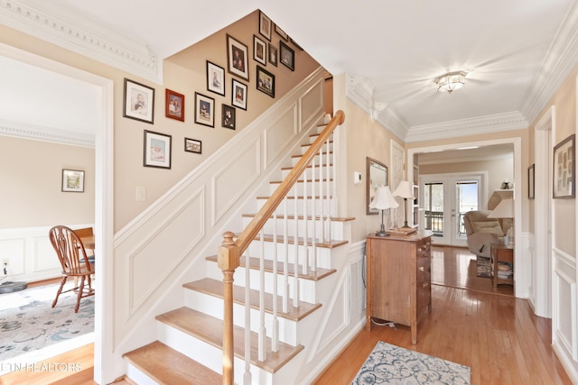 stairs with wood finished floors, a wainscoted wall, french doors, crown molding, and a decorative wall