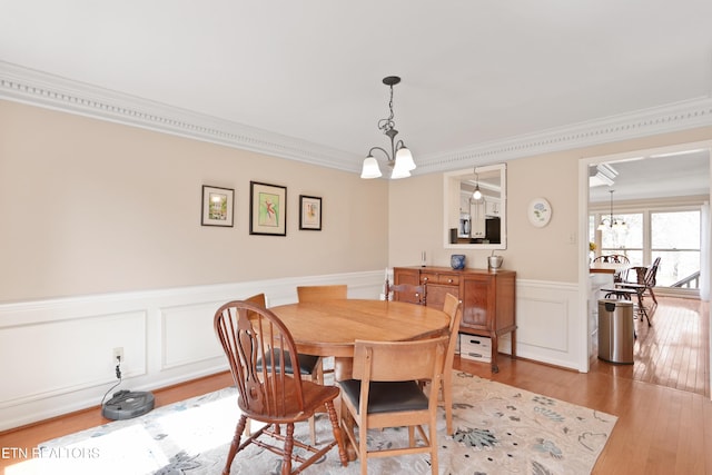 dining room featuring light wood-type flooring, a notable chandelier, a wainscoted wall, and crown molding