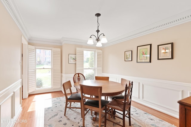 dining space with light wood finished floors, a notable chandelier, crown molding, and a wainscoted wall