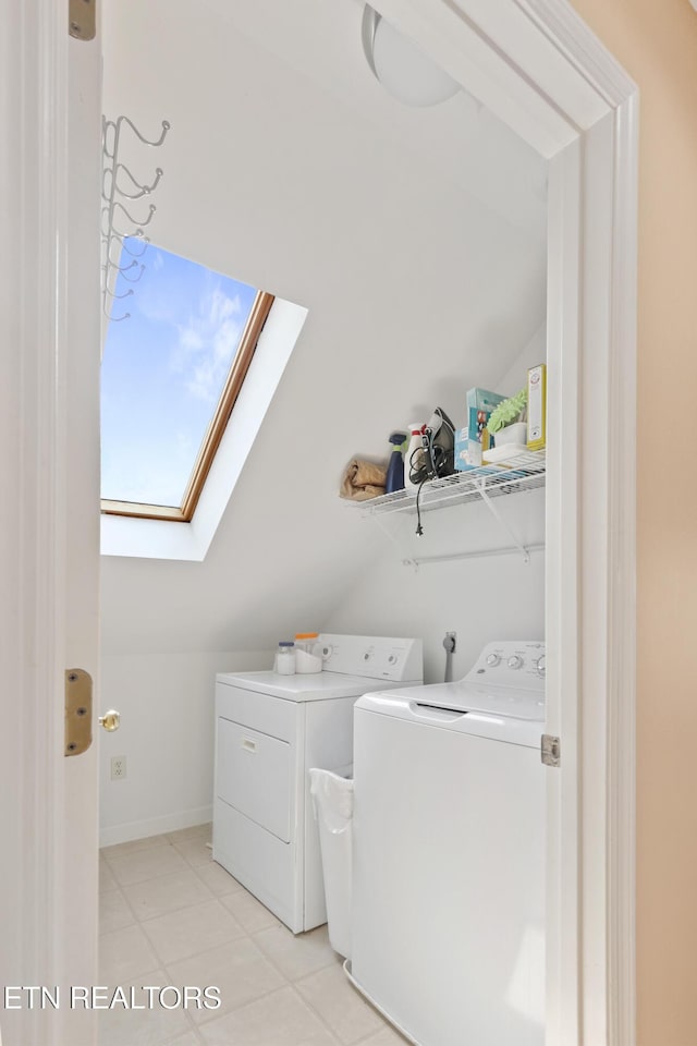 washroom with a skylight, light tile patterned flooring, washing machine and dryer, and laundry area