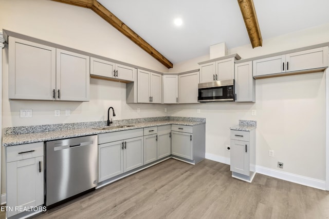 kitchen with baseboards, vaulted ceiling with beams, a sink, stainless steel appliances, and light wood-type flooring