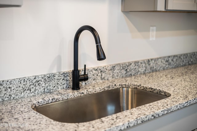 interior details with gray cabinetry, light stone countertops, and a sink