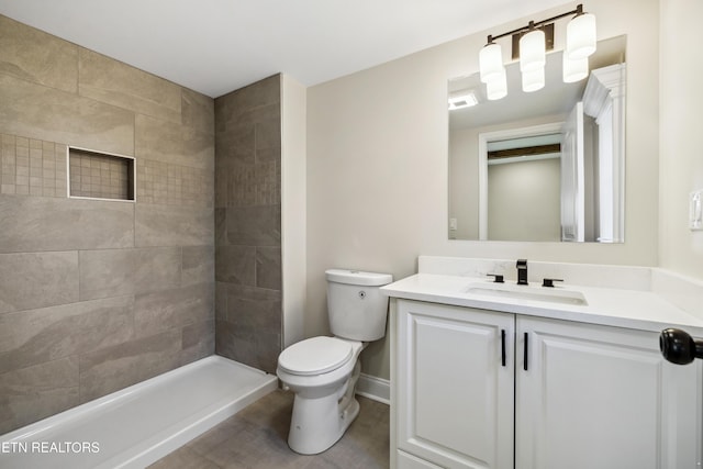 bathroom featuring vanity, toilet, baseboards, and a tile shower