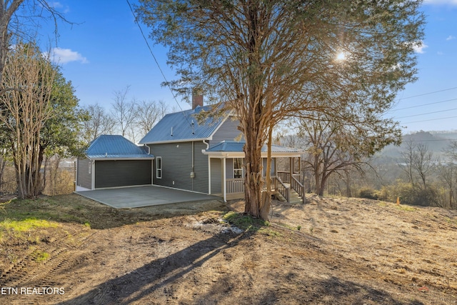 back of house featuring a patio area, driveway, a chimney, and metal roof