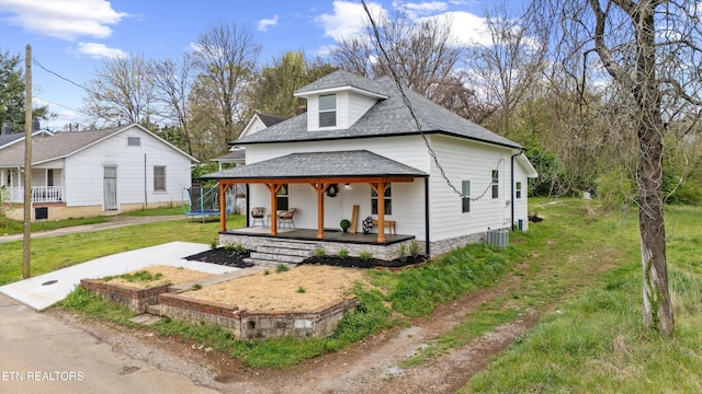 view of front of property featuring a trampoline, a front lawn, a shingled roof, central AC unit, and a porch