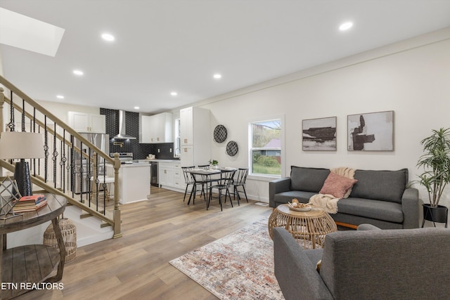 living area featuring light wood-style flooring, a skylight, stairs, and recessed lighting