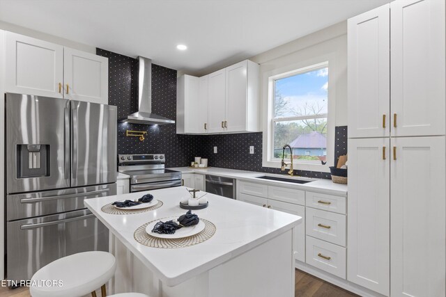 kitchen with a breakfast bar, stainless steel appliances, white cabinetry, a sink, and wall chimney range hood