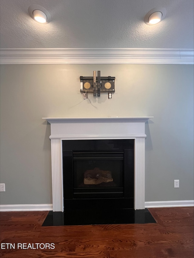 room details with wood finished floors, baseboards, a fireplace with flush hearth, a textured ceiling, and crown molding