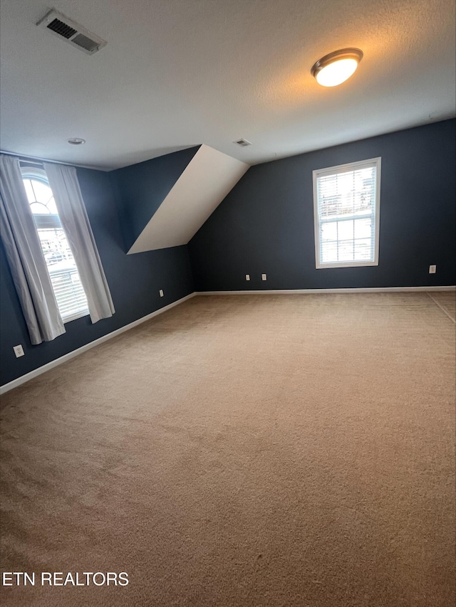 additional living space featuring vaulted ceiling, carpet, visible vents, and a healthy amount of sunlight