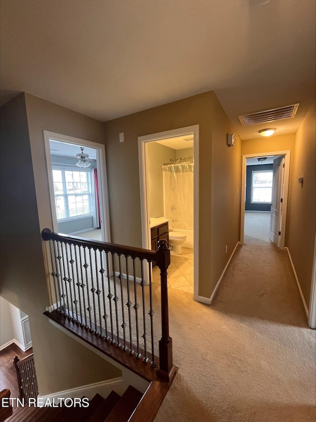 corridor featuring an upstairs landing, visible vents, baseboards, and carpet floors