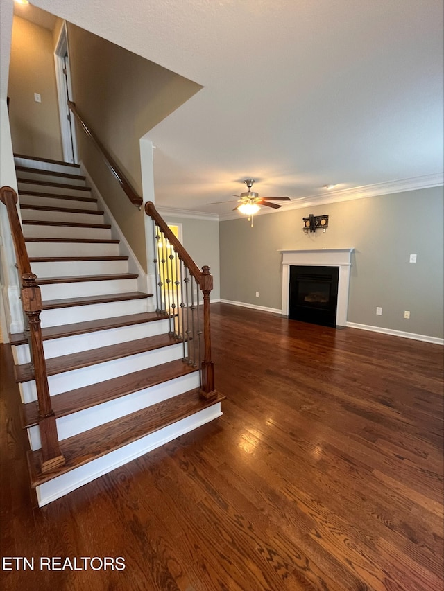 staircase with a ceiling fan, wood finished floors, a fireplace, and ornamental molding