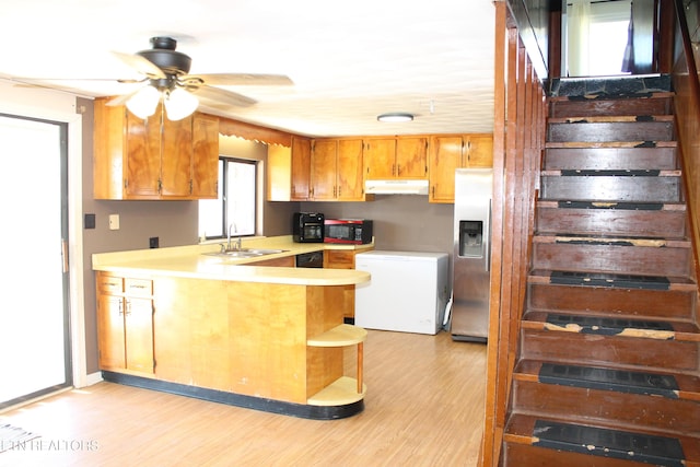 kitchen featuring under cabinet range hood, light countertops, a peninsula, refrigerator, and a sink