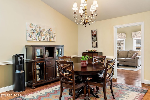 dining room featuring baseboards, lofted ceiling, a notable chandelier, and wood finished floors