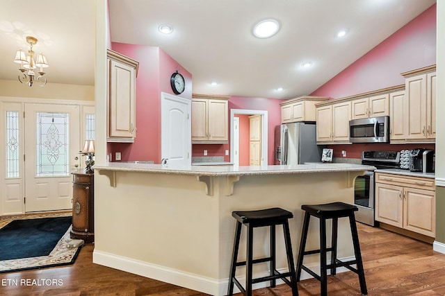 kitchen with a kitchen bar, a peninsula, appliances with stainless steel finishes, and wood finished floors