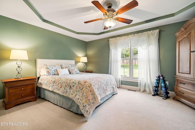 bedroom with a ceiling fan, visible vents, baseboards, a raised ceiling, and light colored carpet