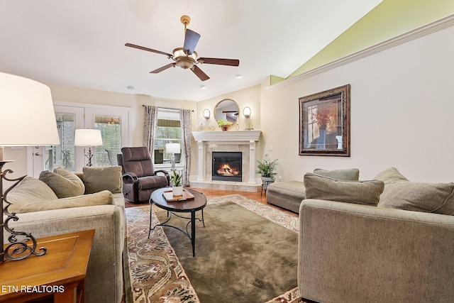 living area with ceiling fan, wood finished floors, a tiled fireplace, and vaulted ceiling