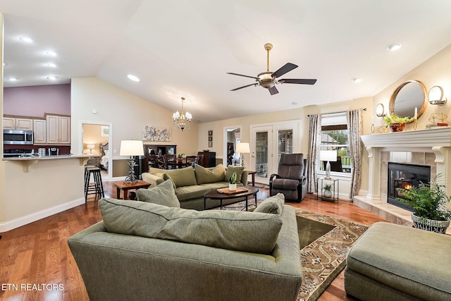 living room featuring baseboards, a tiled fireplace, vaulted ceiling, ceiling fan with notable chandelier, and wood finished floors