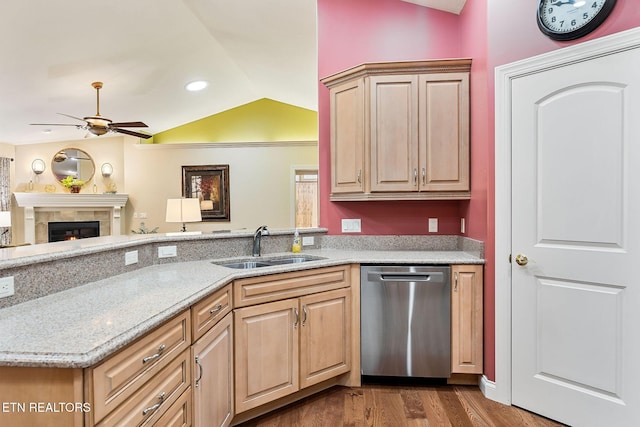 kitchen with dishwasher, lofted ceiling, light stone counters, a tile fireplace, and a sink