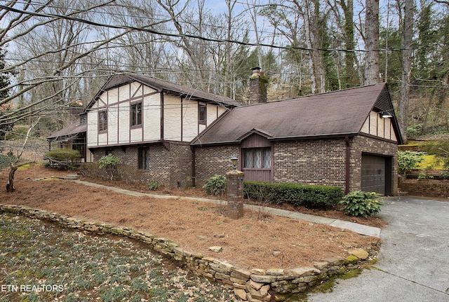 tudor-style house featuring brick siding, roof with shingles, stucco siding, a chimney, and a garage