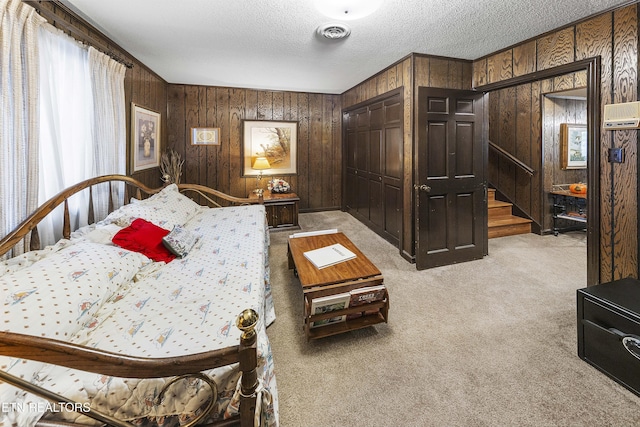 bedroom with wooden walls, light colored carpet, visible vents, and a textured ceiling