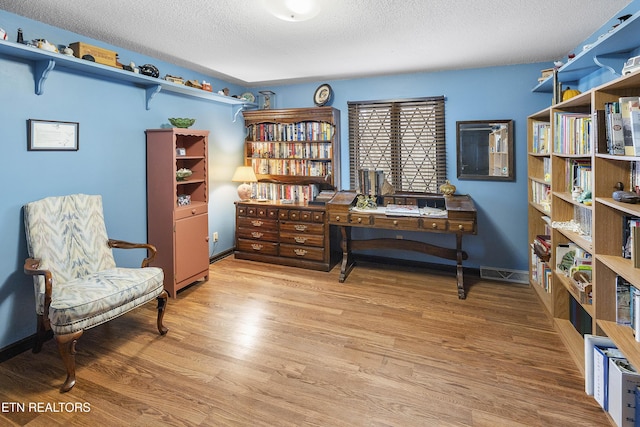 living area with visible vents, baseboards, a textured ceiling, and wood finished floors