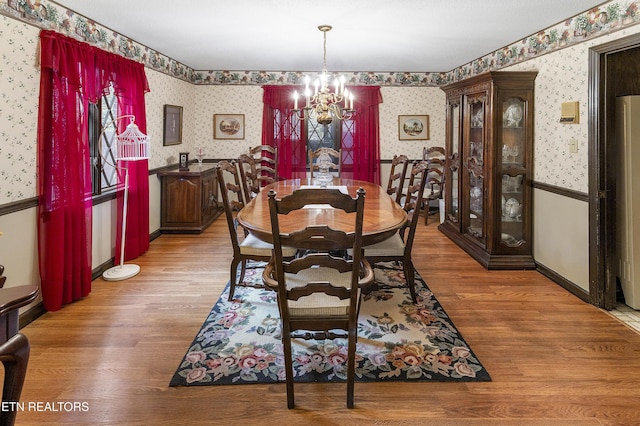 dining room with a wainscoted wall, a notable chandelier, wood finished floors, and wallpapered walls