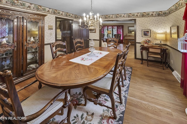 dining area featuring light wood-style flooring, an inviting chandelier, wainscoting, wallpapered walls, and baseboards