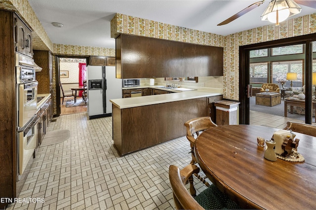 kitchen featuring white appliances, a peninsula, light countertops, and wallpapered walls