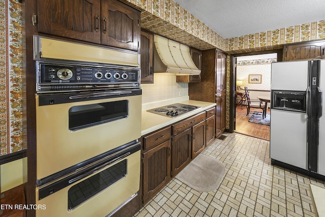 kitchen featuring range hood, wallpapered walls, light countertops, stainless steel electric stovetop, and white fridge with ice dispenser