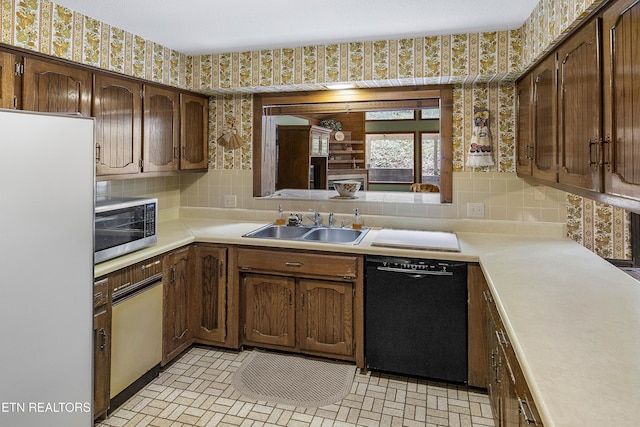 kitchen featuring wallpapered walls, freestanding refrigerator, a sink, black dishwasher, and stainless steel microwave